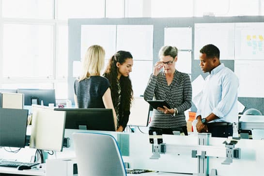 Four people reviewing notes on a tablet in a workplace